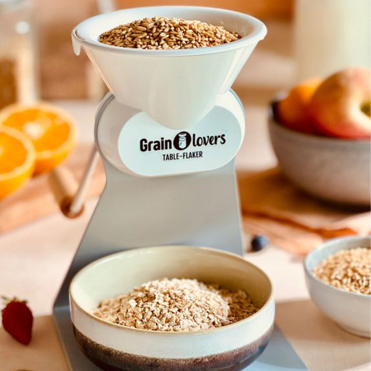 Grainlovers Table-Flaker Handflocker mit Getreidekörnern gefüllt, frische Flocken in Schale, Tischszene mit Obst